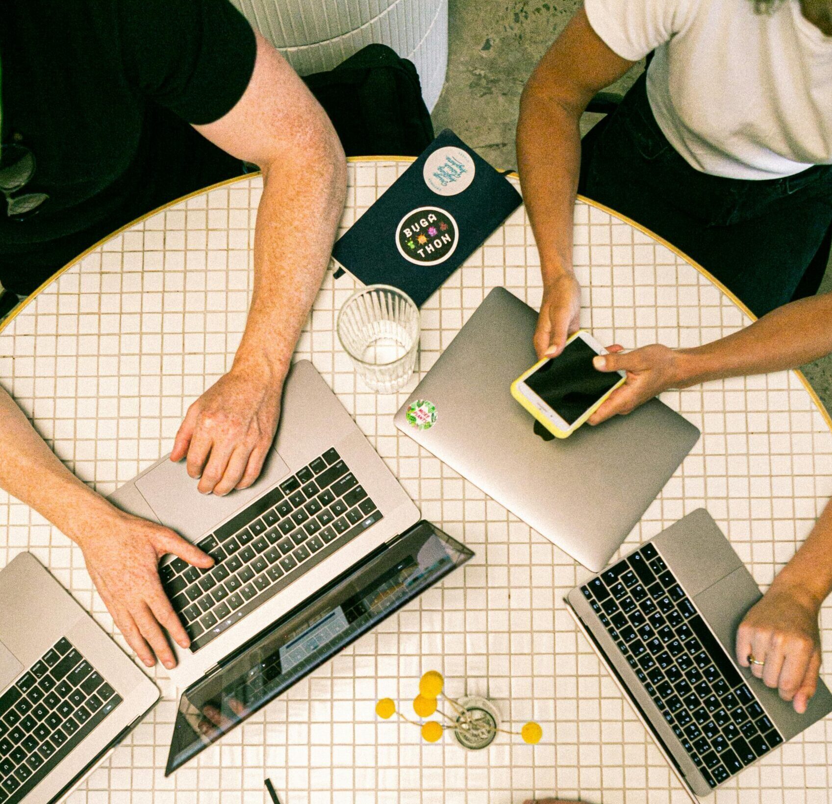 Top view of a team collaborating with laptops, phones, and notes in a modern office.